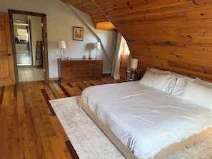 Een slaapkamer met een houten plafond, een groot bed, een kaptafel en een nachtkastje met lampen.