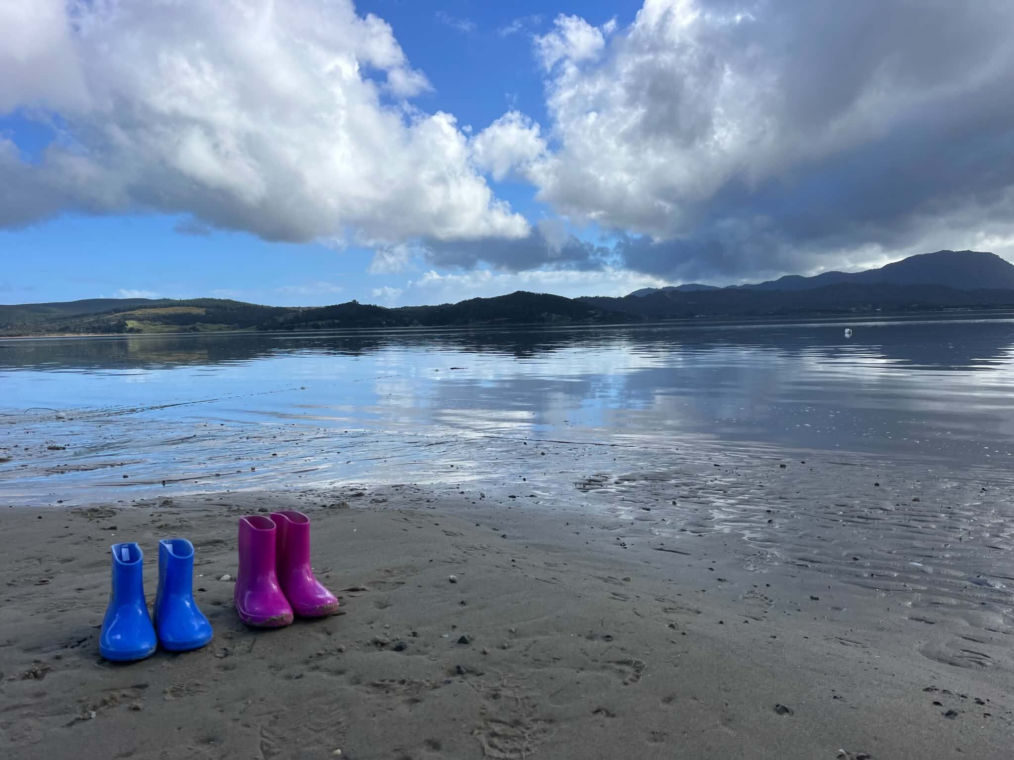 A beach with footprints leading to a pair of blue and pink boots.