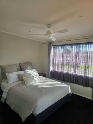 A bedroom with a bed, a ceiling fan, a window with curtains, and a view of the outdoors.