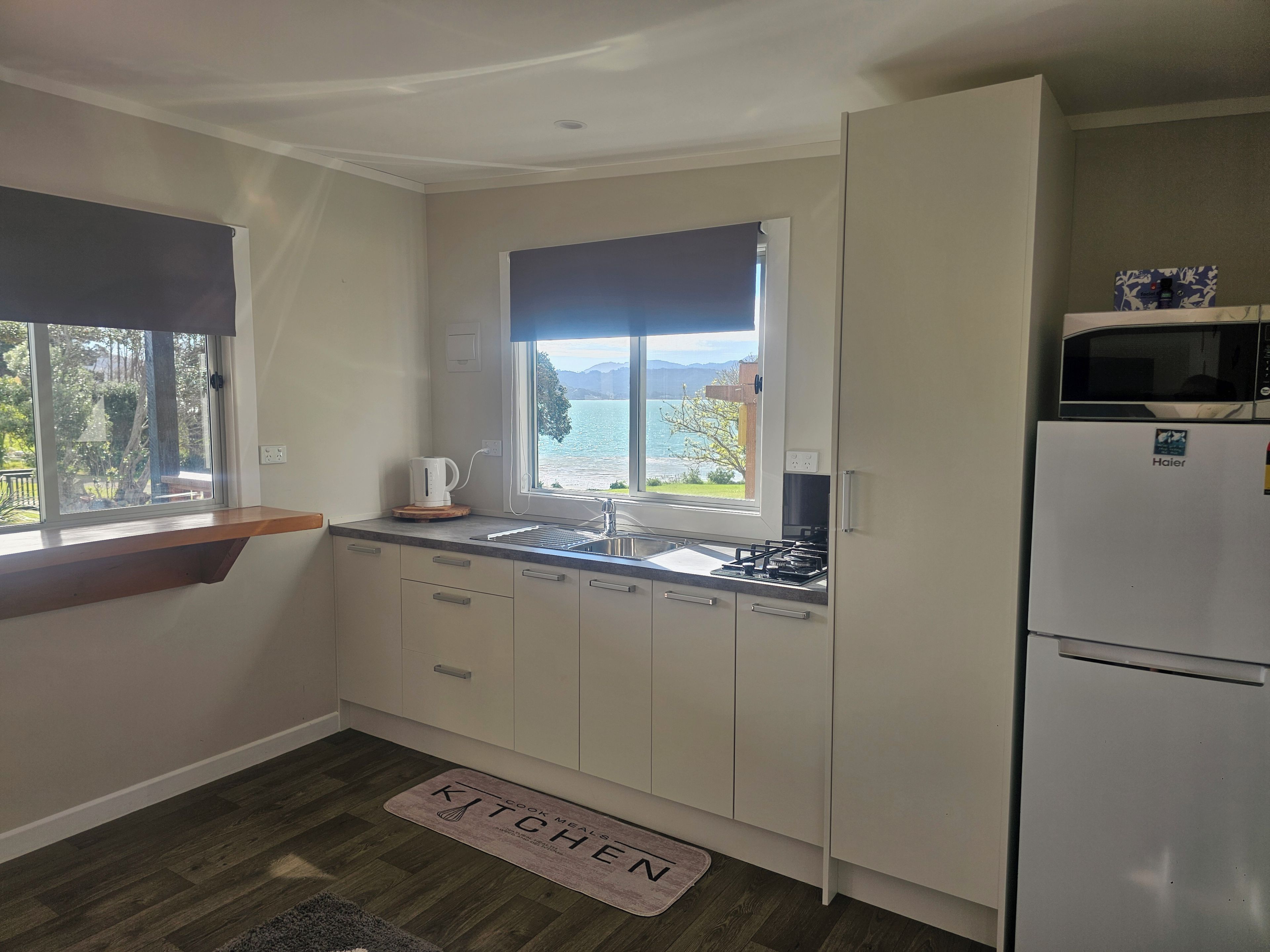 A compact kitchen with a view of a lake, a white refrigerator, and a coffee maker on the counter.
