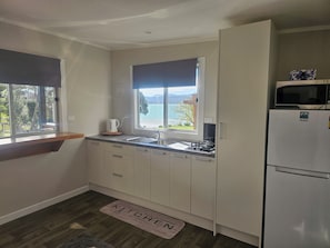 Une cuisine compacte avec vue sur un lac, un réfrigérateur blanc et une machine à café posée sur le plan de travail.