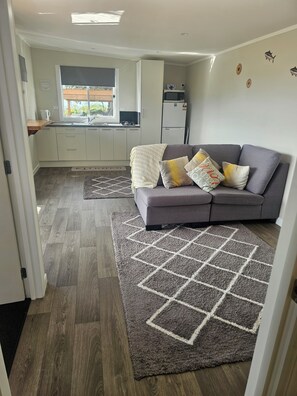 A modern living room with a grey sofa, a patterned rug, and a kitchen area in the background.