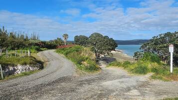 A gravel path leading to a beach with a warning sign, surrounded by greenery and trees.
