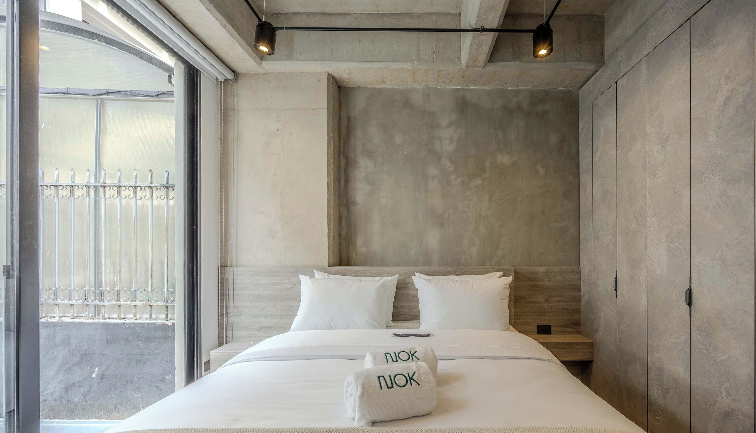 Una habitación de hotel con una cama grande, vistas a la calle y una pared de hormigón.