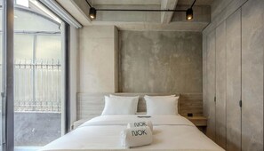 Quarto de hotel com uma cama grande, vista da rua e uma parede de concreto.