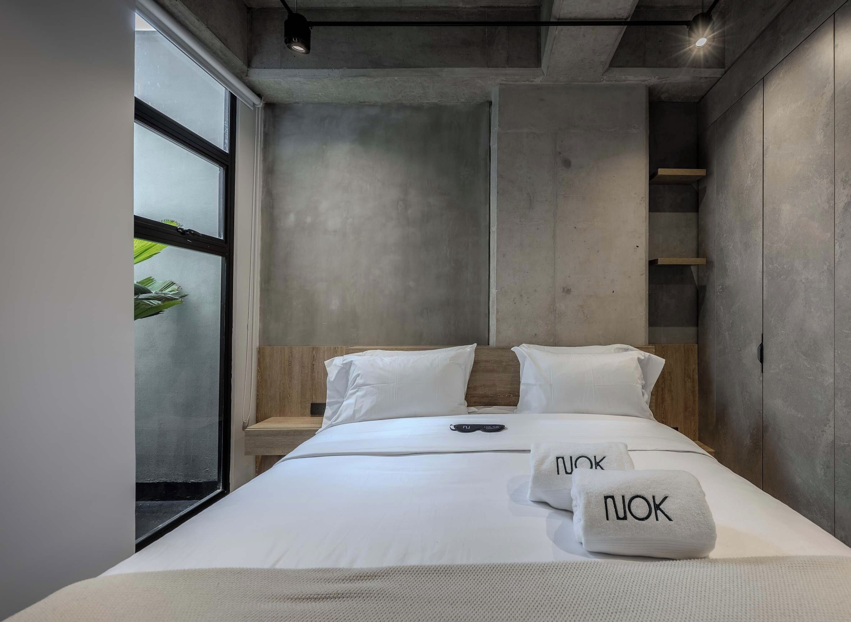 Una habitación de hotel moderna con una cama grande, una mesita de noche y un ventanal con vistas.