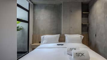 Una habitación de hotel moderna con una cama grande, una mesita de noche y un ventanal con vistas.