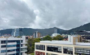 Un paysage urbain avec des bâtiments modernes, une montagne en arrière-plan et un ciel nuageux.