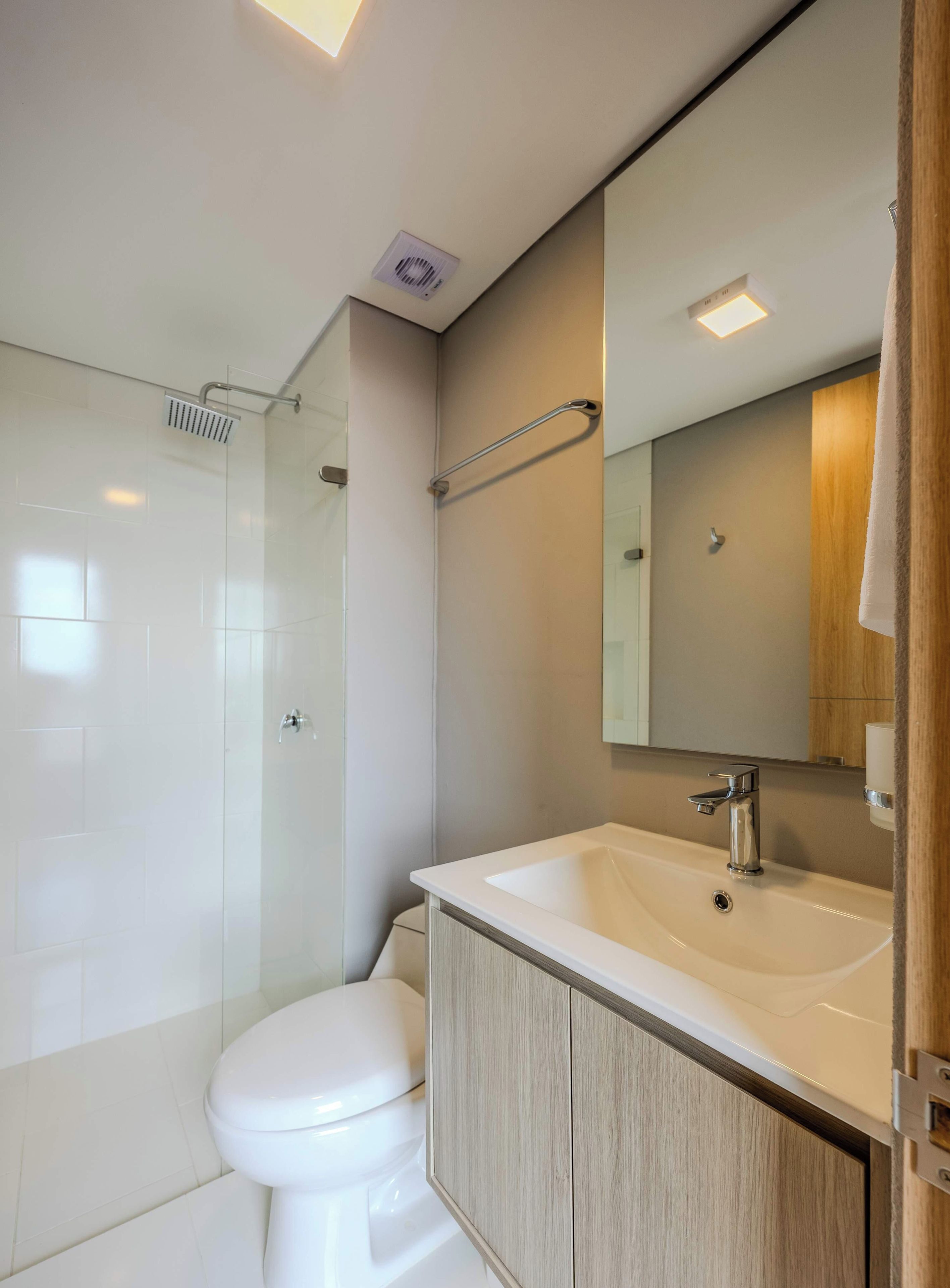 Un baño moderno con cabina de ducha de vidrio, inodoro blanco, tocador de madera con lavamanos y espejo.