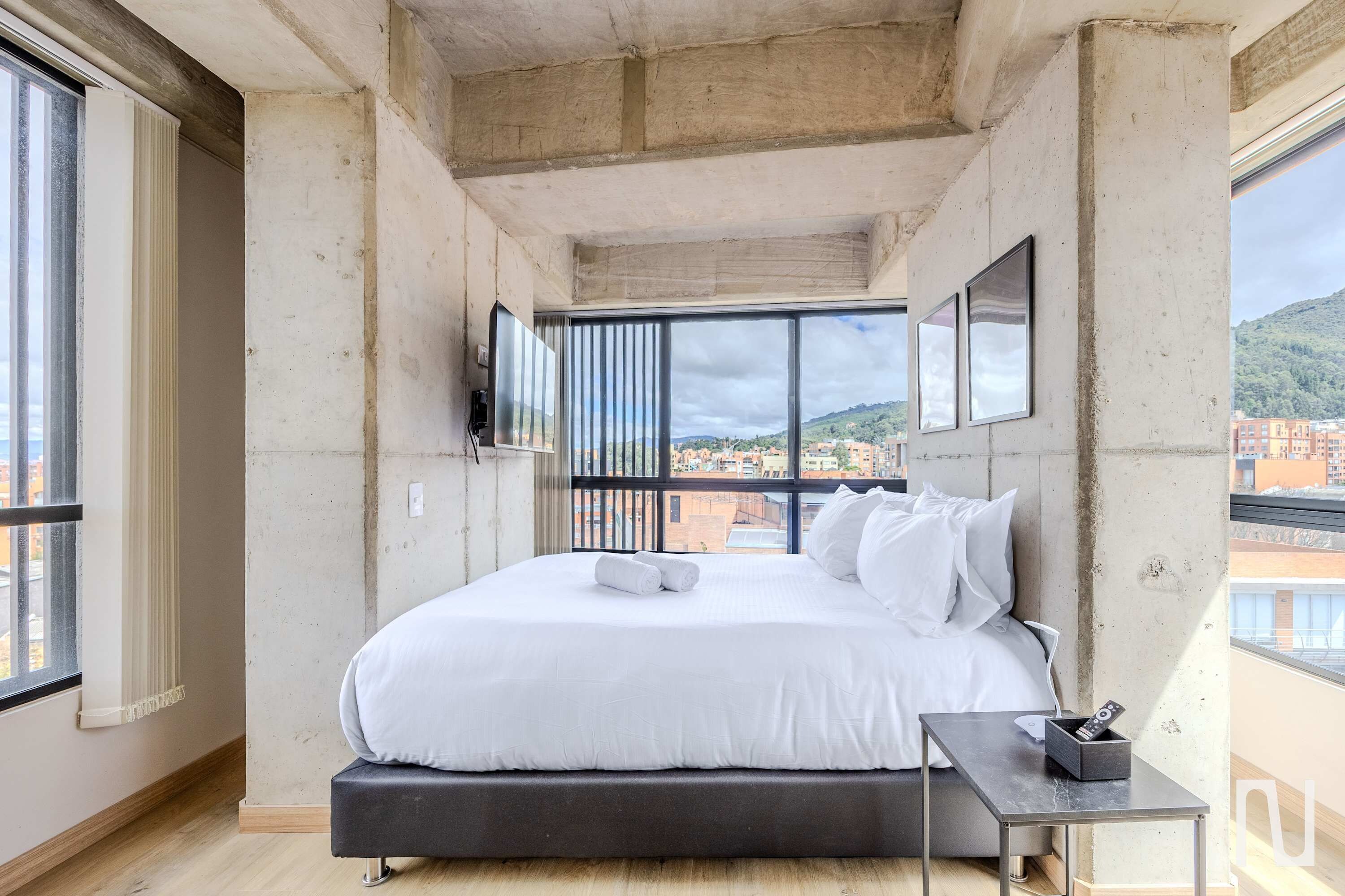 Un dormitorio moderno con una cama grande, una mesita pequeña y un televisor montado en la pared.