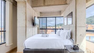 Un dormitorio moderno con una cama grande, una mesita pequeña y un televisor montado en la pared.