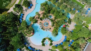 Vista aérea de un resort con piscina central, rodeado de palmeras y sombrillas azules.