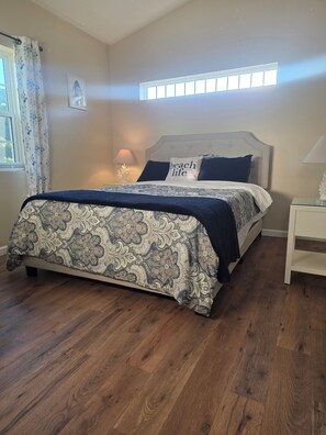 Un dormitorio con cama, mesita de noche, ventana con cortinas y lámpara de pared.