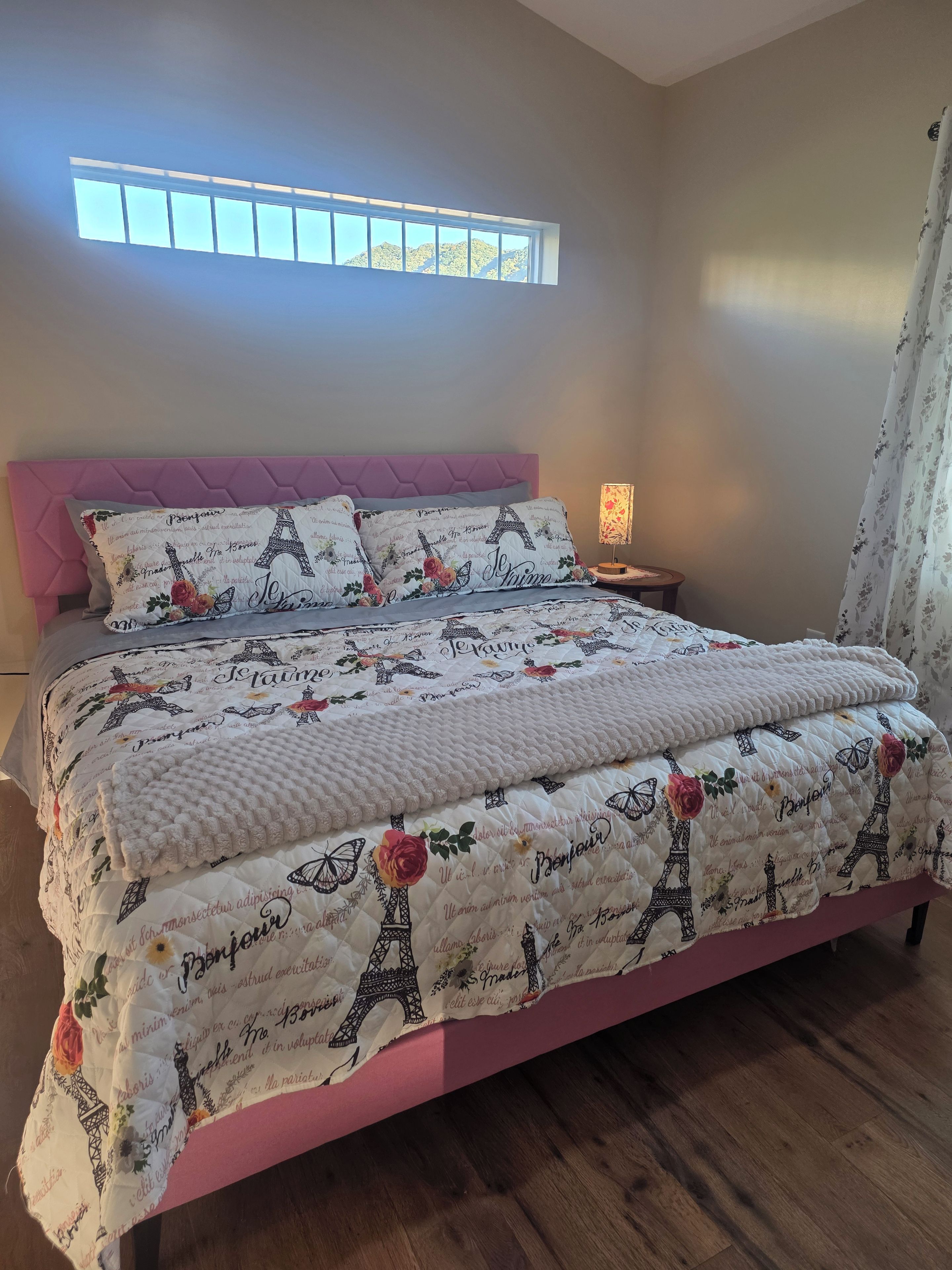 Une chambre à coucher avec un lit, une table de chevet, une fenêtre et un rideau.
