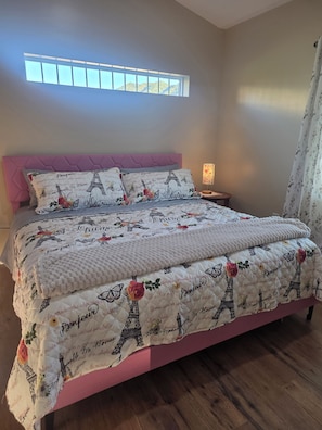 Ein Schlafzimmer mit einem Bett, einem Nachttisch, einem Fenster und einem Vorhang.