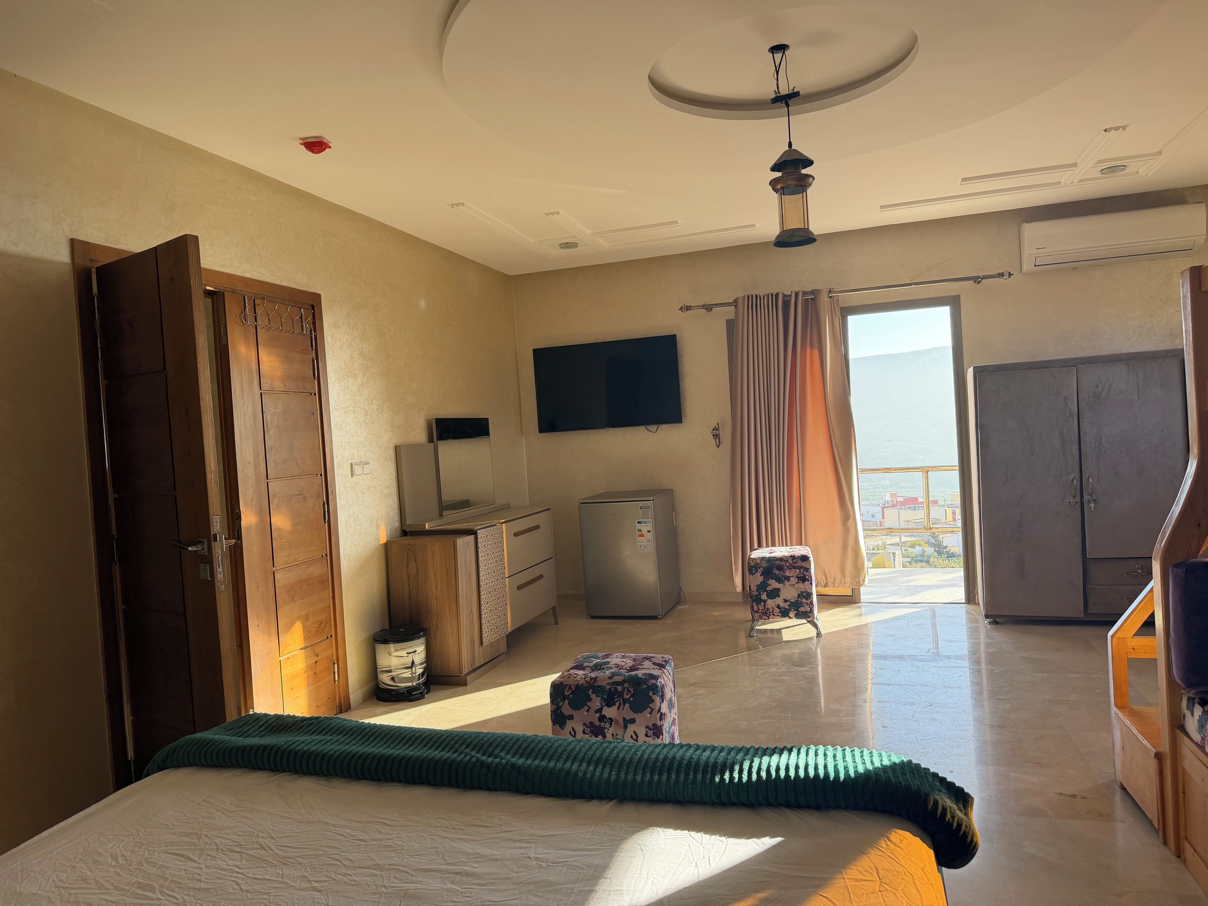 Ein Hotelzimmer mit Bett, Schreibtisch, Fernseher, Kleiderschrank und Blick aus dem Fenster.