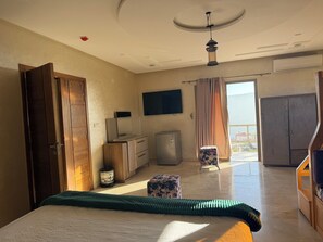 Quarto de hotel com cama, escrivaninha, televisão, guarda-roupa e vista pela janela.