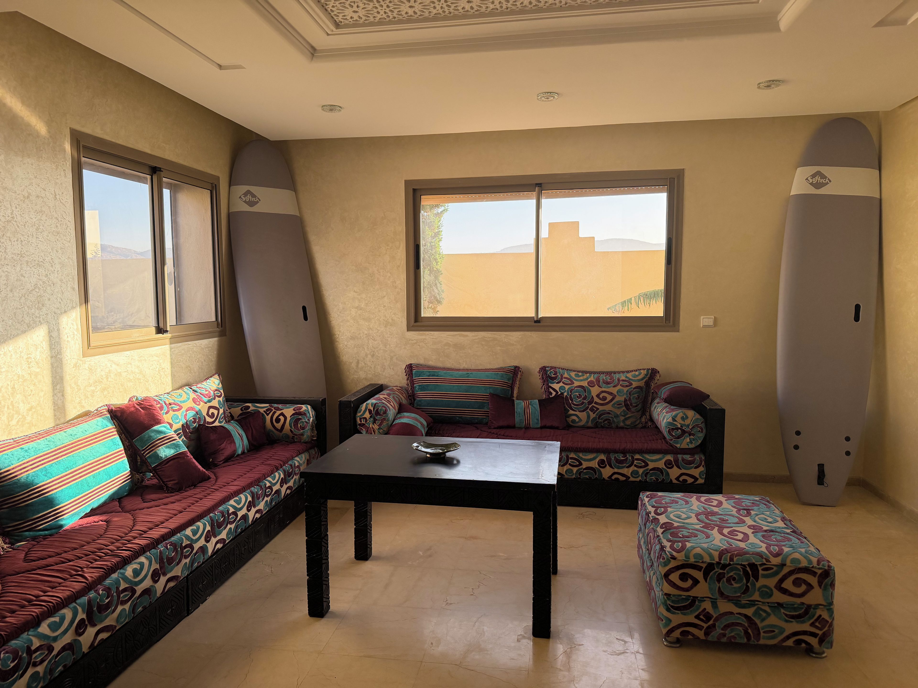 Ein Zimmer mit einer Sofagarnitur, einem Tisch und zwei Surfbrettern an der Wand.