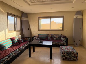 Quarto com sofá, uma mesa e dois pranchas de surf encostados na parede.