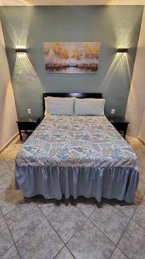 Una cama con colcha estampada, dos mesitas de noche, un cuadro colgado en la pared y dos lámparas de pared.