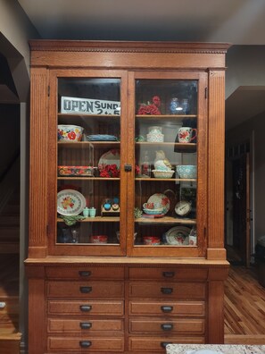 Een houten kast met glazen deuren, gevuld met divers keukengerei en decoratieve objecten.