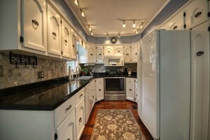 Una cucina con mobili bianchi, un piano di lavoro nero, un forno in acciaio inossidabile e un frigorifero.