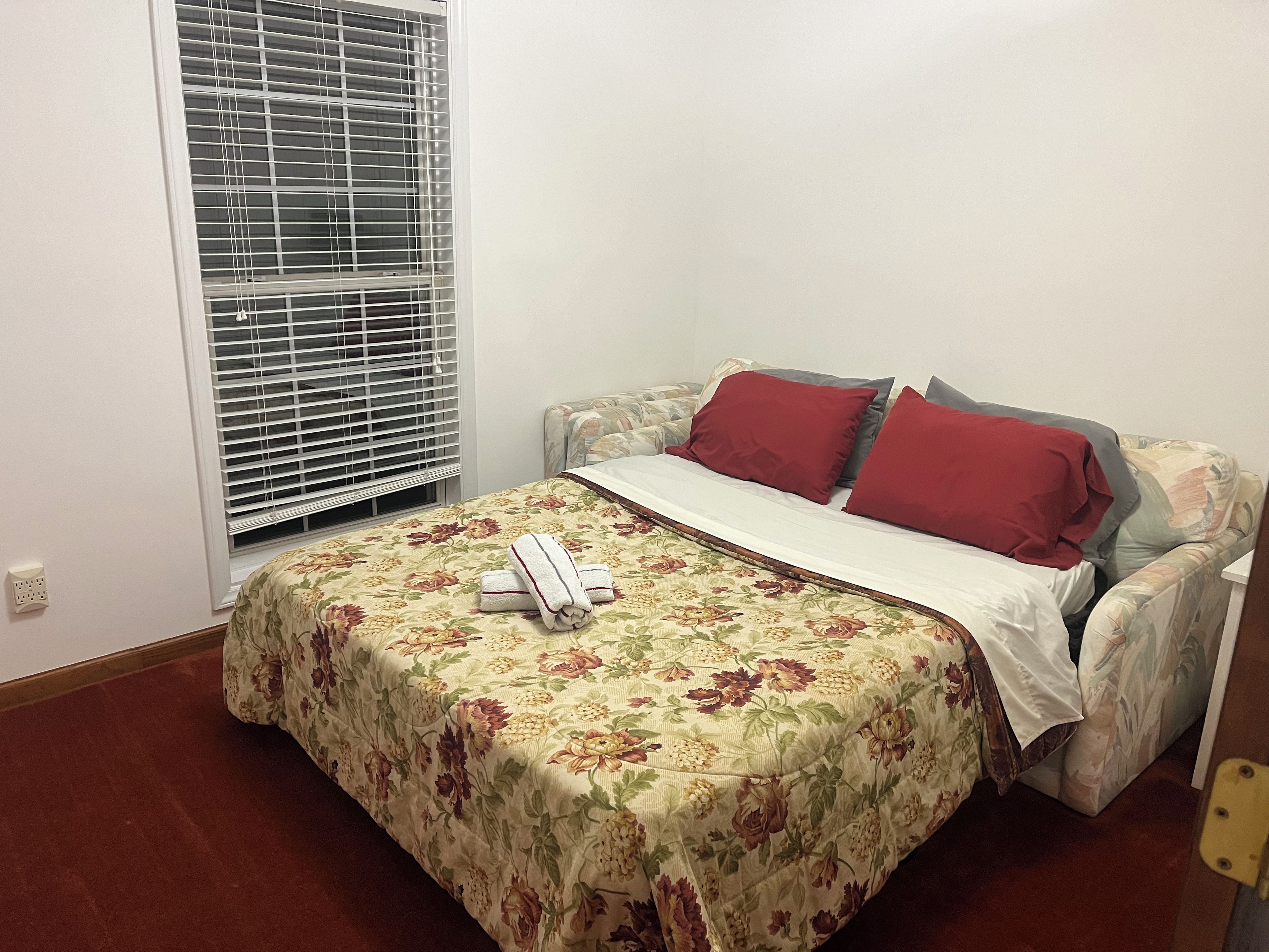 Un letto singolo con una coperta a fiori, due cuscini rossi e una coperta bianca.