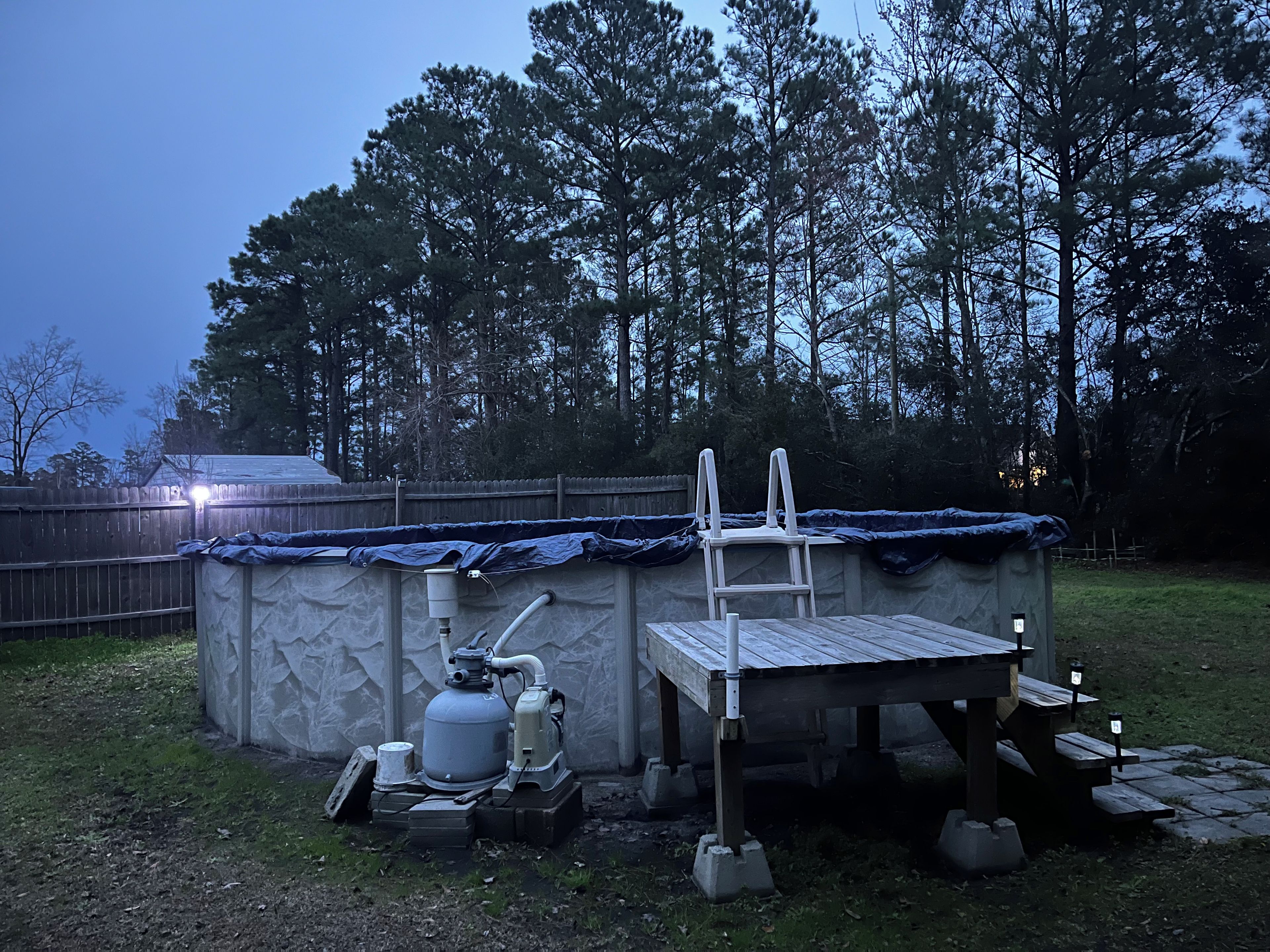 A small outdoor structure with a table and chairs, a ladder, and a propane tank.