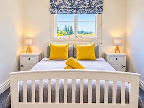A bedroom with a bed, two bedside tables, a window with a view, and a patterned valance.
