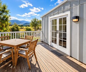 A wooden deck with a table and chairs, a white exterior wall, and a view of the landscape.
