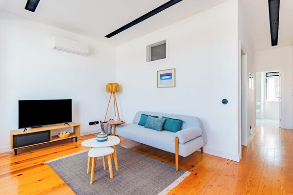 A modern living room with a flat-screen TV, a light blue sofa, a small round table, and a wooden floor. - Urban Haven 2BR Modern Retreat (Lisbon)