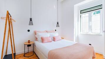 A bedroom with a bed, two pendant lights, a wooden ladder, a small round table, and a window with blinds.