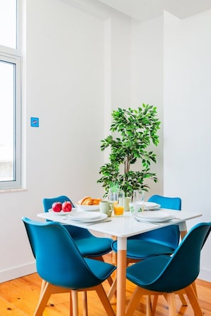 A dining area with a white table, blue chairs, a potted plant, and breakfast items. - Urban Haven 2BR Modern Retreat (Lisbon)