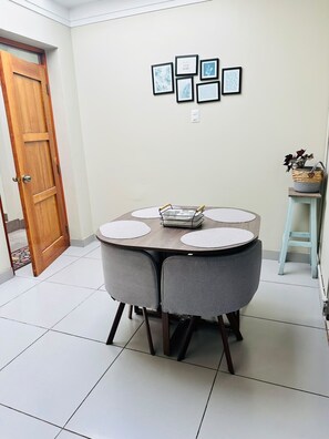 A dining area with a round table, grey chairs, and a small stool with a plant. - Yuraqtampu Centenario (Cusco)