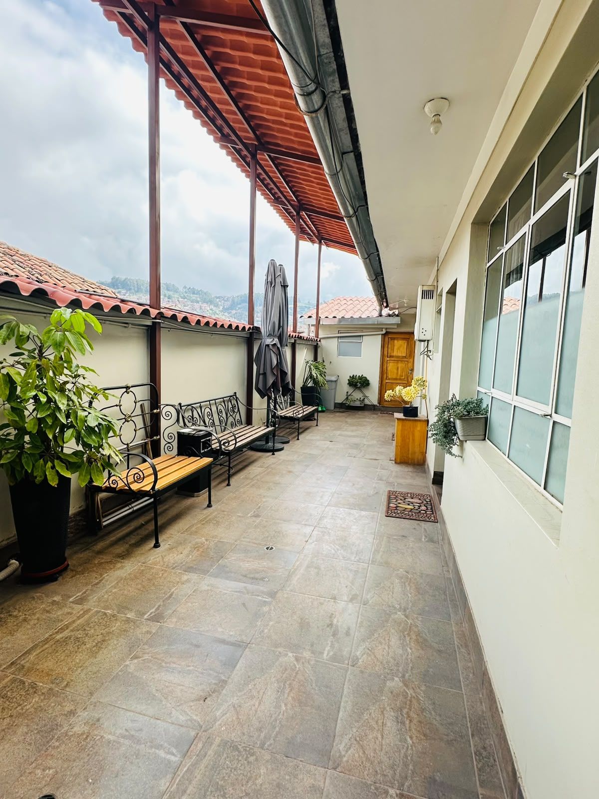A covered outdoor area with a bench, potted plants, and a view of the sky.