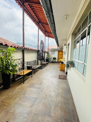 A covered outdoor area with a bench, potted plants, and a view of the sky. - Yuraqtampu Centenario (Cusco)