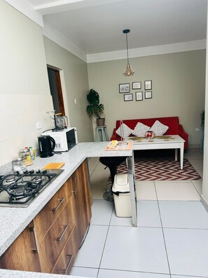 A compact kitchen with a gas stove, a coffee maker, and a dining area with a red sofa and a table. - Yuraqtampu Centenario (Cusco)