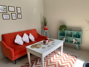 A living room with a red sofa, white cushions, a white coffee table with decorative items, a patterned rug, and a teal shelving unit with small figurines. - Yuraqtampu Centenario (Cusco)