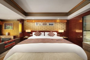 Quarto de hotel com uma cama grande, uma escrivaninha com cadeira, telefone e janela com persianas.