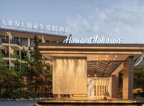 Um hotel Howard Johnson com fachada moderna, entrada coberta e um espelho d'água à frente.