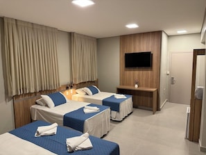 Een hotelkamer met twee bedden, een aan de muur bevestigde televisie en een houten nachtkastje.
