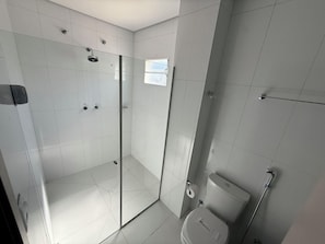 Een badkamer met een douchecabine van glas, een toilet en een klein raam.