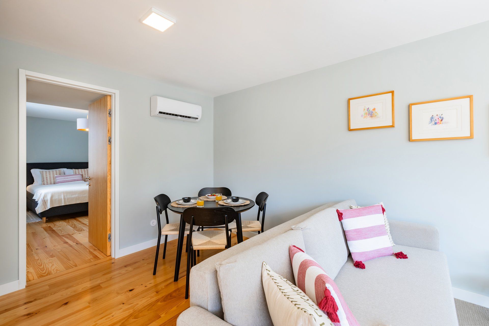 Una sala moderna con un sofá, una mesa de comedor con sillas, una cama al fondo y dos cuadros en la pared.