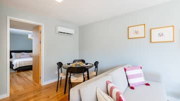 Una sala moderna con un sofá, una mesa de comedor con sillas, una cama al fondo y dos cuadros en la pared.