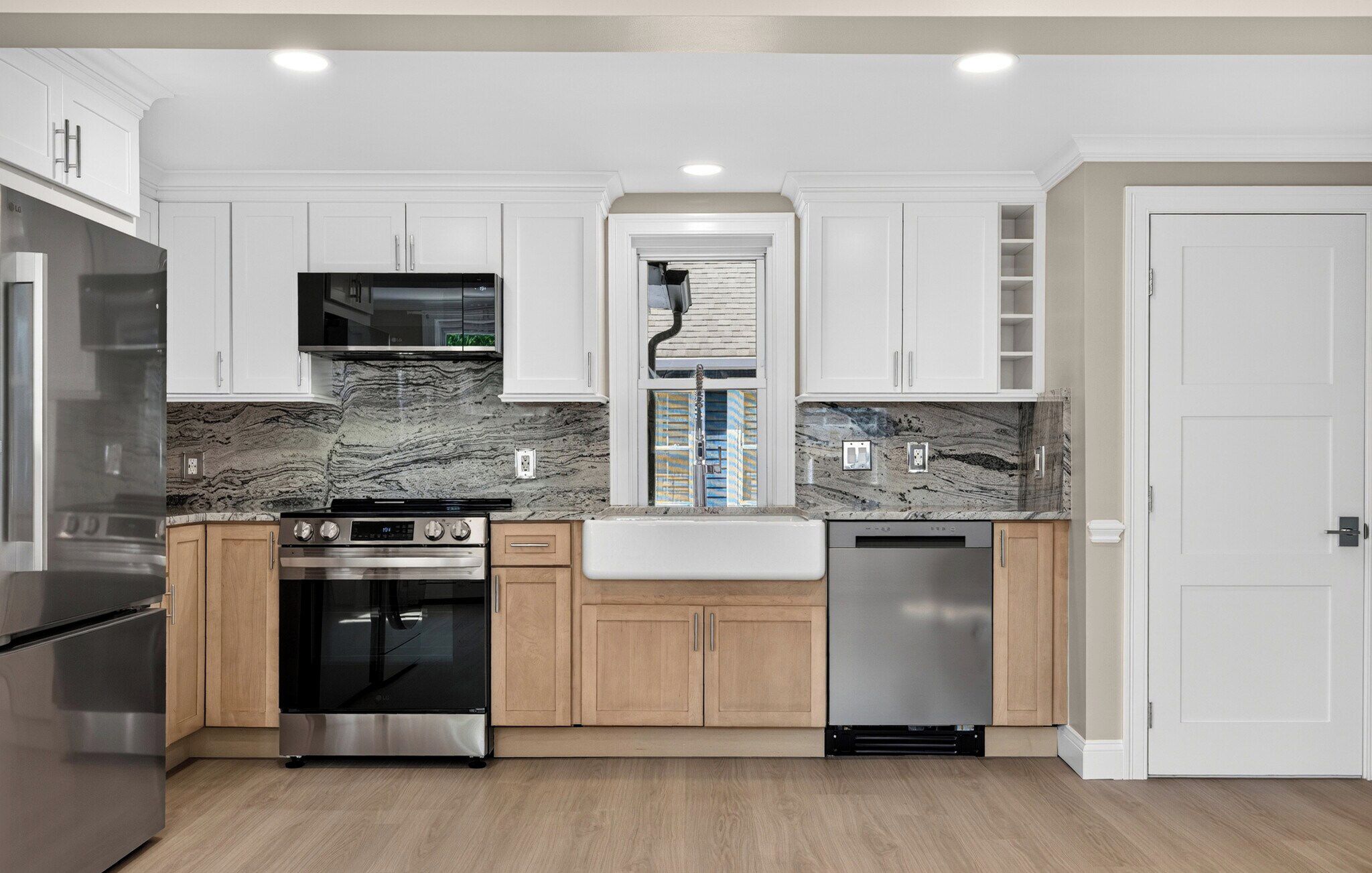 A modern kitchen with white cabinetry, a marble backsplash, stainless steel appliances, and a wooden floor.