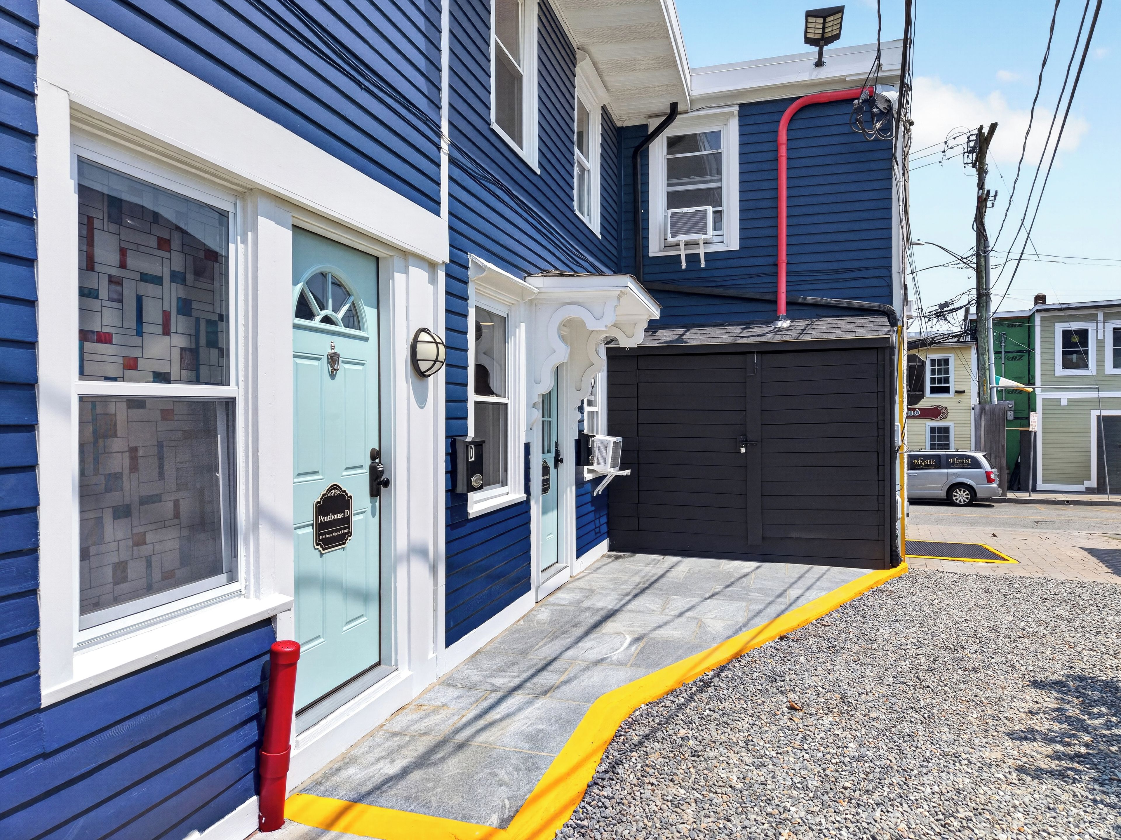A building with a garage door, a blue door with a window, and a small porch area.