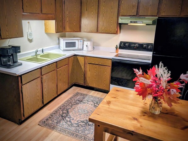 Una cocina con armarios de madera, microondas, cafetera, estufa y una mesa con un florero.