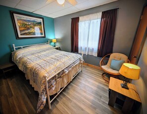 A bedroom with a bed, a chair, a lamp, a nightstand, and a window with curtains.