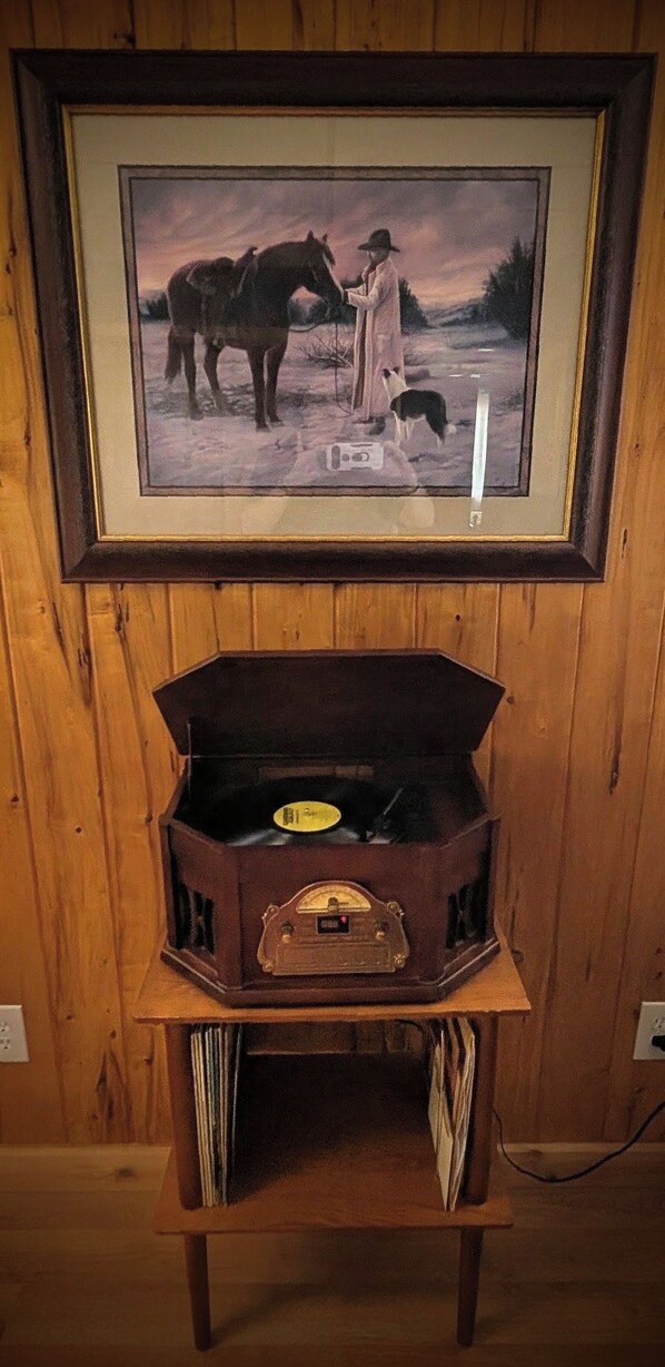 A framed painting of a person with a horse and dog on a snowy landscape. Below the painting, there is a vintage radio on a wooden cabinet.