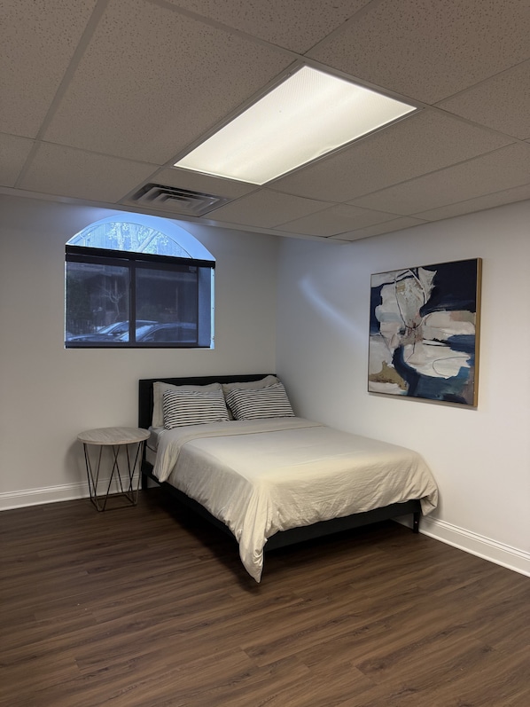A bedroom with a bed, a round side table, a window, and a painting on the wall. - Family Sized Apt. — in the Heart of Hyde Park ! (Chicago)